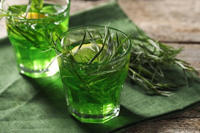 Photo of Glasses of refreshing tarragon drink with lemon slices on wooden table, closeup