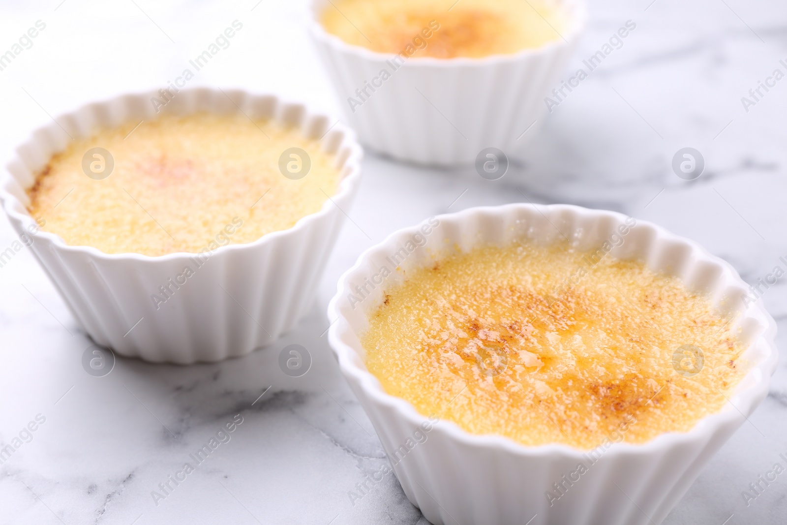 Photo of Delicious creme brulee in bowls on white marble table, closeup