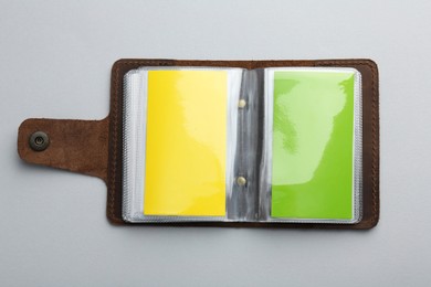 Leather business card holder with colorful cards on light grey background, top view