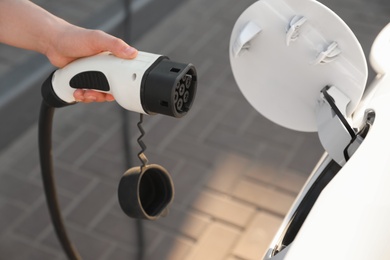 Photo of Woman inserting plug into electric car socket at charging station, closeup