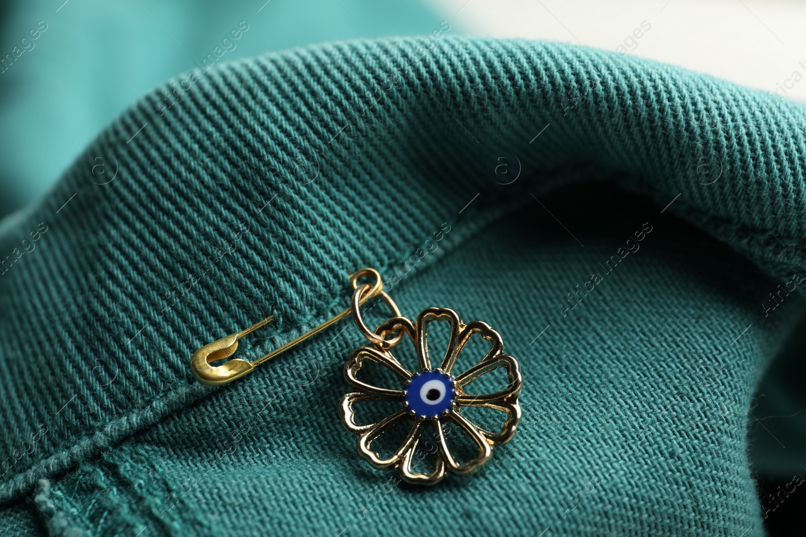 Photo of Evil eye safety pin on denim clothing, closeup