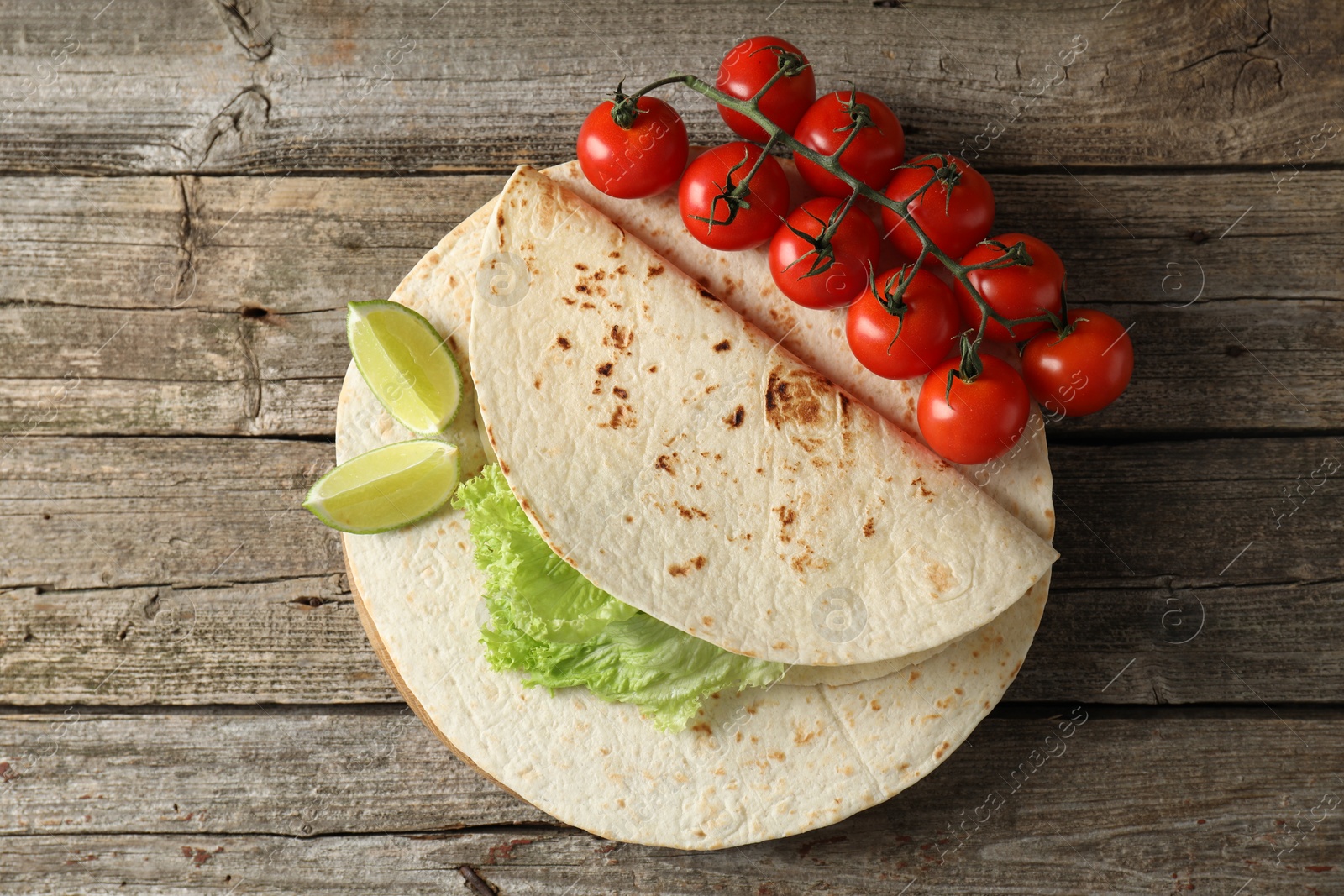 Photo of Tasty homemade tortillas, tomatoes, lime and lettuce on wooden table, top view