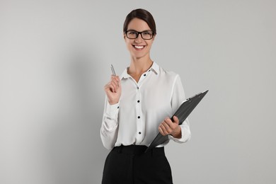 Happy secretary with clipboard and pen on light grey background