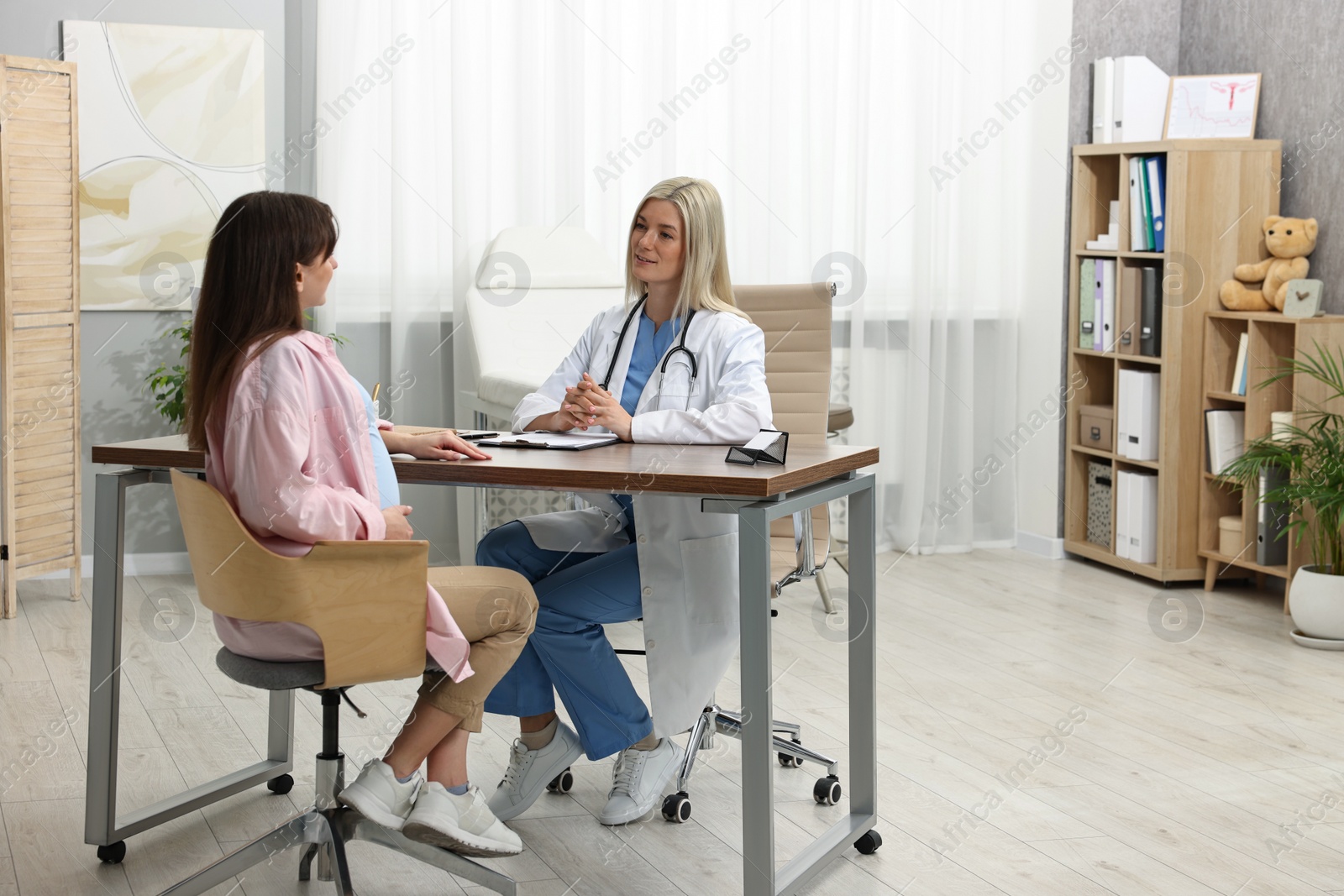 Photo of Smiling doctor consulting pregnant patient at table in clinic