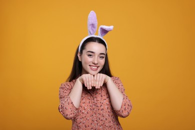 Photo of Happy woman wearing bunny ears headband on orange background. Easter celebration