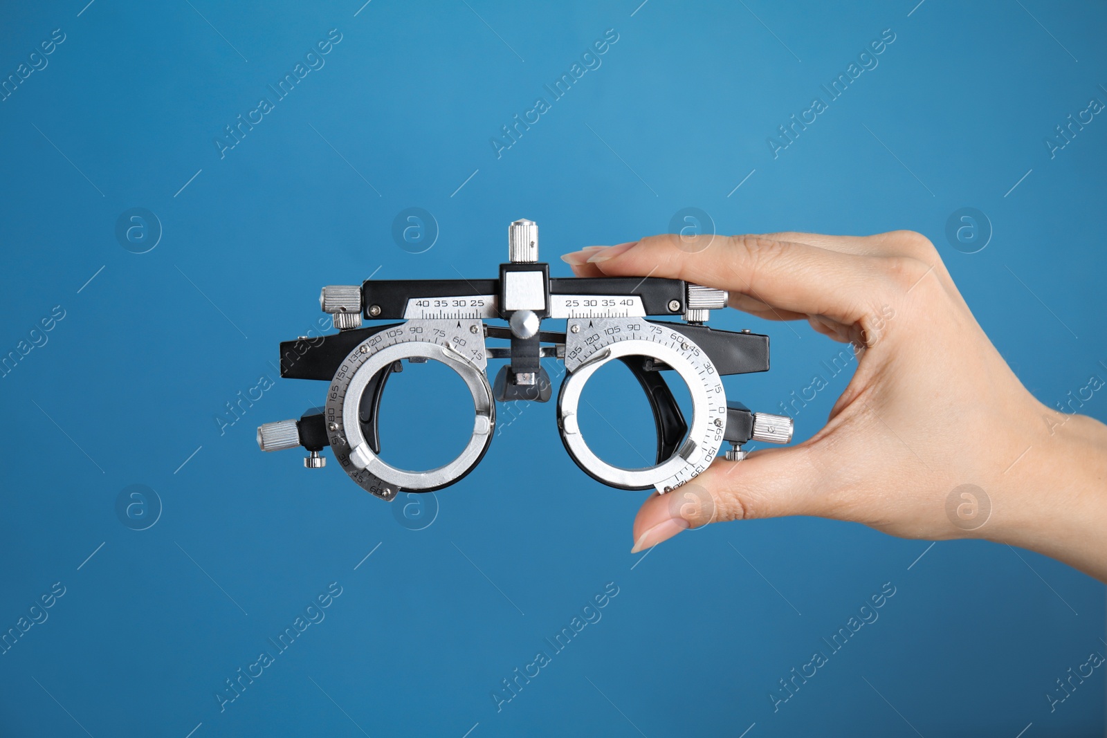 Photo of Woman holding trial frame on blue background, closeup. Ophthalmologist tool