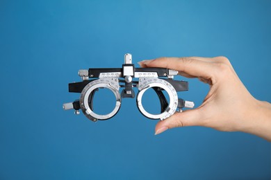 Photo of Woman holding trial frame on blue background, closeup. Ophthalmologist tool