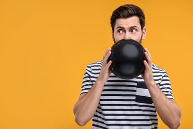 Man inflating black balloon on yellow background. Space for text