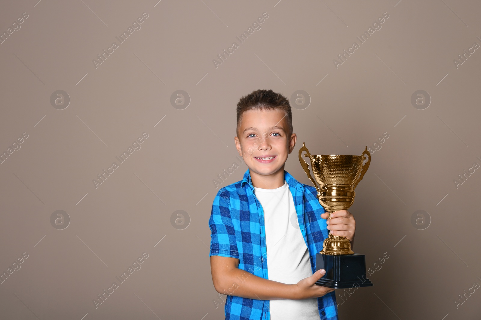 Photo of Happy boy with golden winning cup on beige background. Space for text