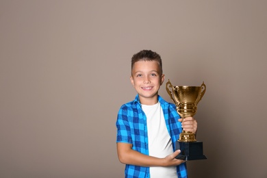 Happy boy with golden winning cup on beige background. Space for text