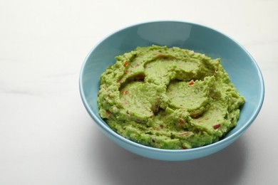 Photo of Bowl with delicious fresh guacamole on white table, space for text