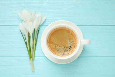 Photo of Cup of morning coffee and crocuses on light blue wooden table, flat lay