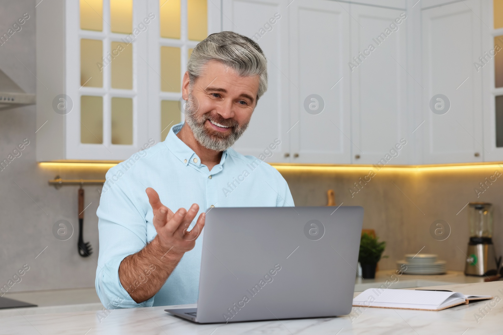 Photo of Man waving hello during video chat via laptop at home