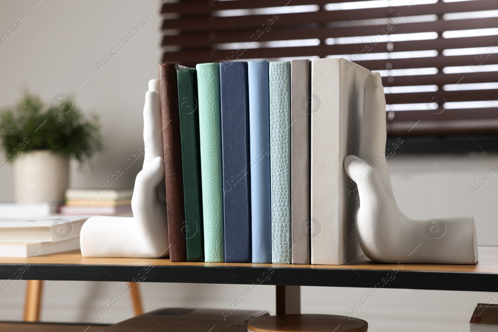 Photo of Beautiful hand shaped bookends with books on shelf indoors