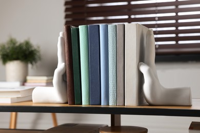 Photo of Beautiful hand shaped bookends with books on shelf indoors