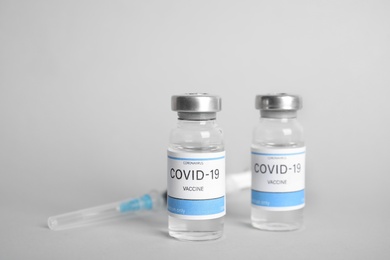 Vials with coronavirus vaccine and syringe on light background