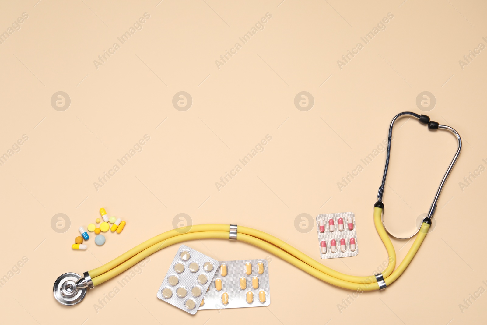 Photo of Stethoscope and pills on beige background, flat lay. Space for text