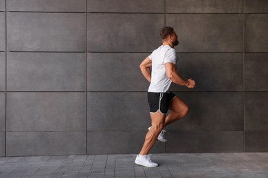 Young man running near building outdoors. Space for text