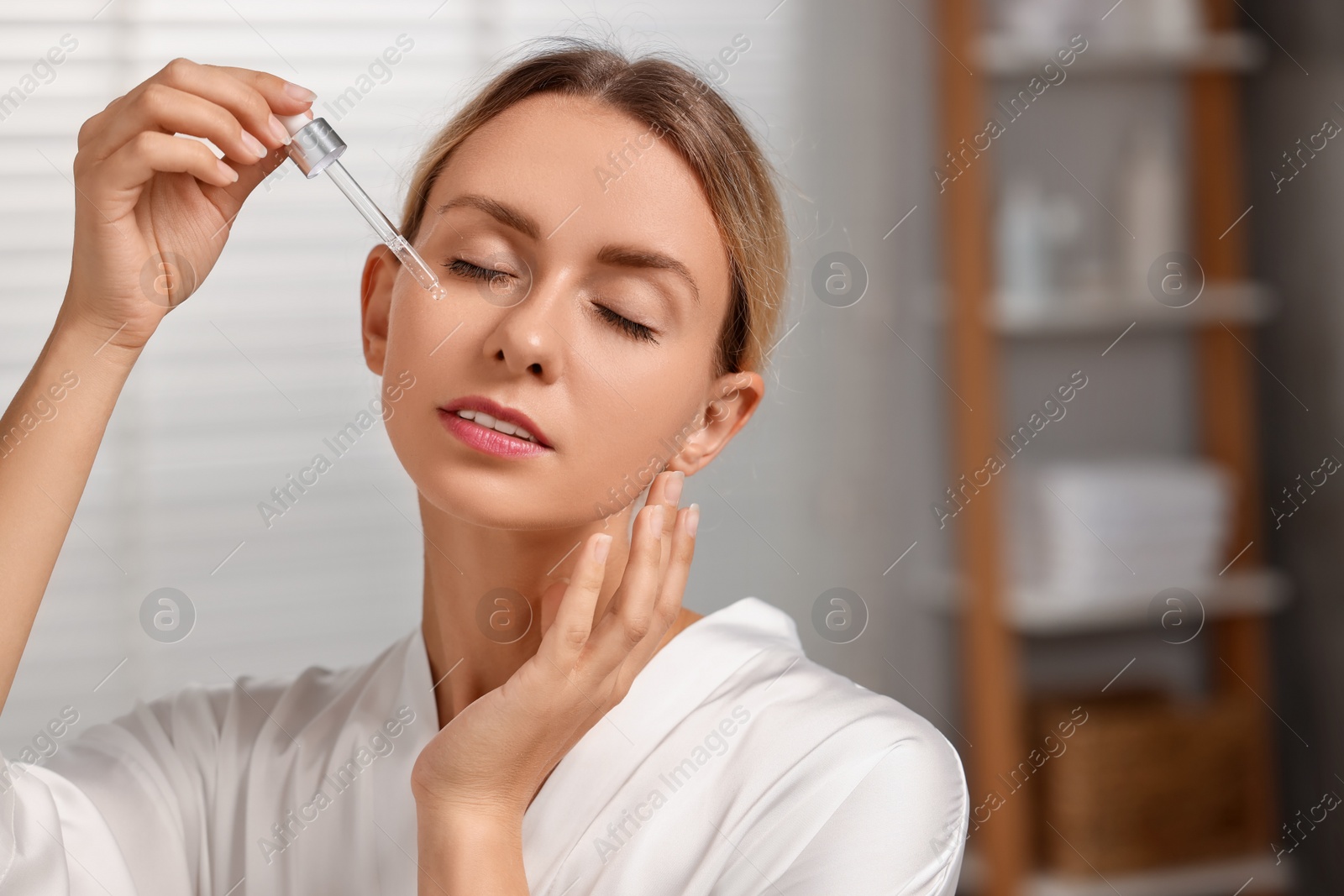 Photo of Beautiful woman applying cosmetic serum onto her face in bathroom, space for text