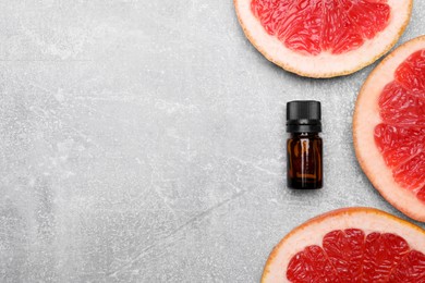 Photo of Bottle of essential oil with grapefruit slices on grey table, flat lay. Space for text