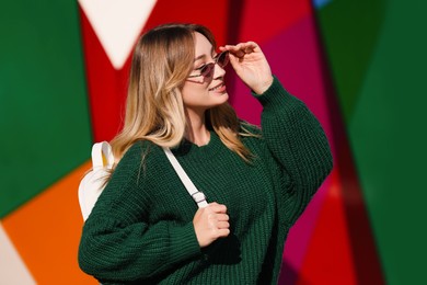 Young woman with stylish backpack near color wall