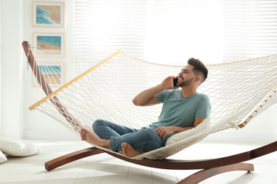 Photo of Young man talking on mobile phone in hammock at home