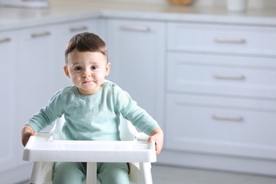 Photo of Cute little baby sitting in high chair at kitchen. Space for text