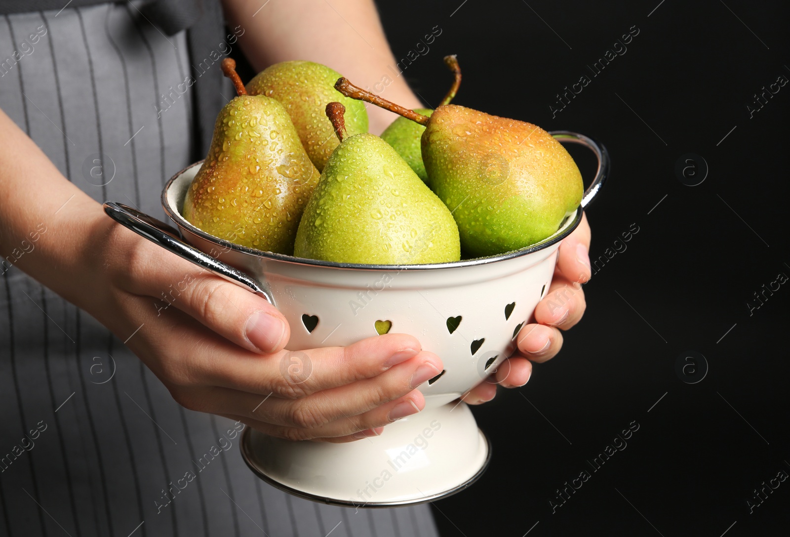 Photo of Woman holding colander with ripe pears on black background, closeup