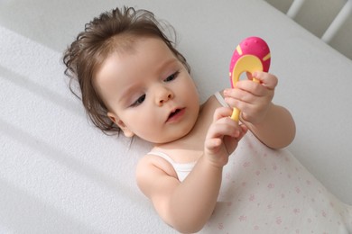 Photo of Cute little baby with toothbrush in comfortable crib, top view