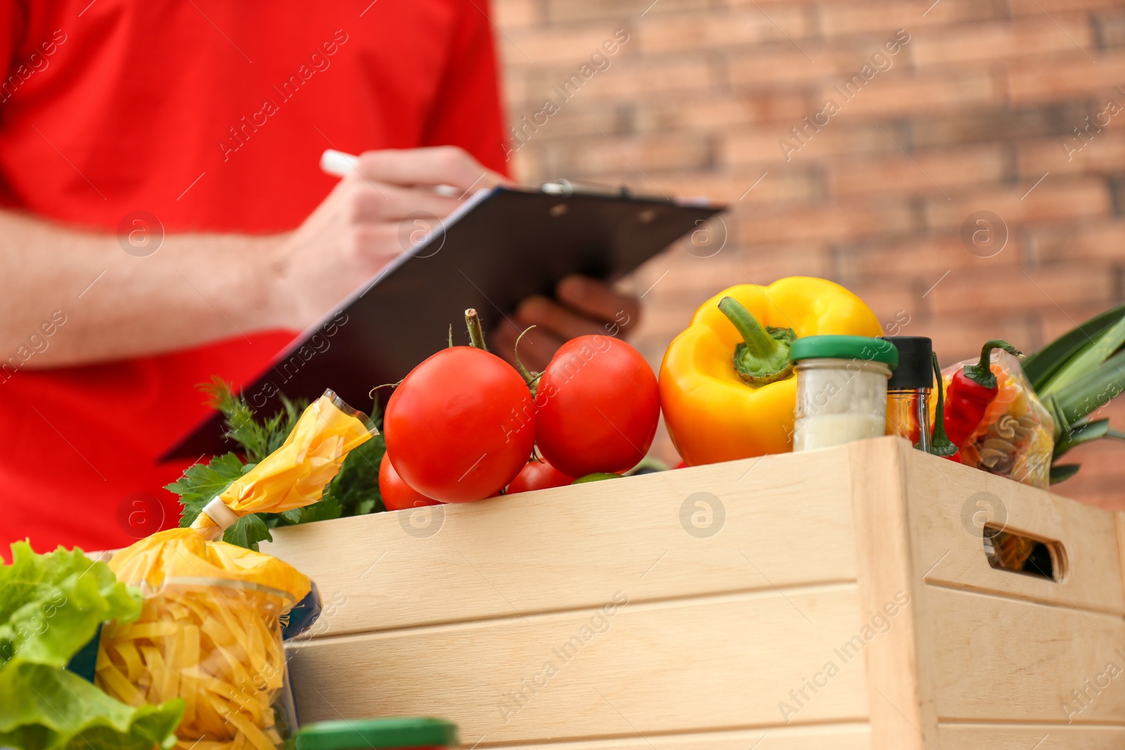 Photo of Different fresh products and blurred man with clipboard on background. Food delivery service