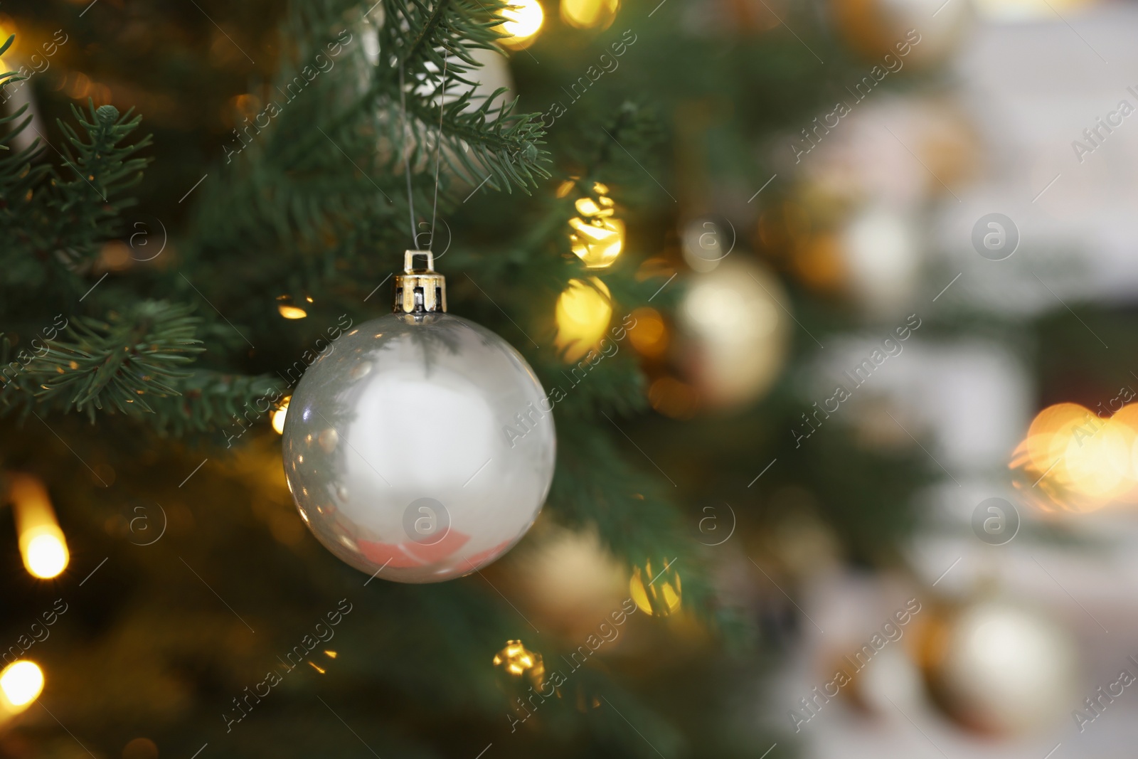 Photo of Beautiful silver Christmas ball hanging on fir tree branch against blurred background, closeup. Space for text