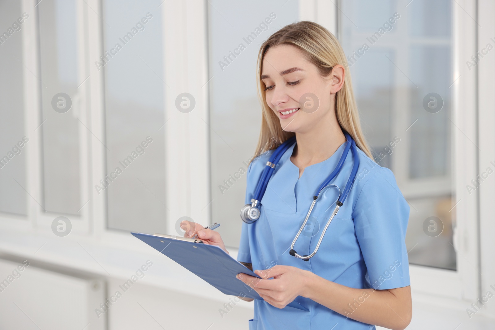 Photo of Young intern wearing uniform with clipboard in university hall, space for text