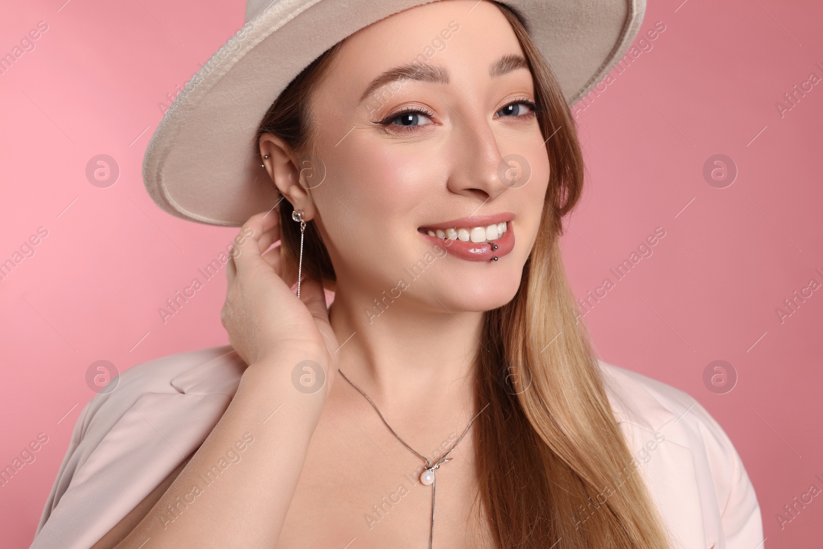 Photo of Young woman with lip and ear piercings on pink background