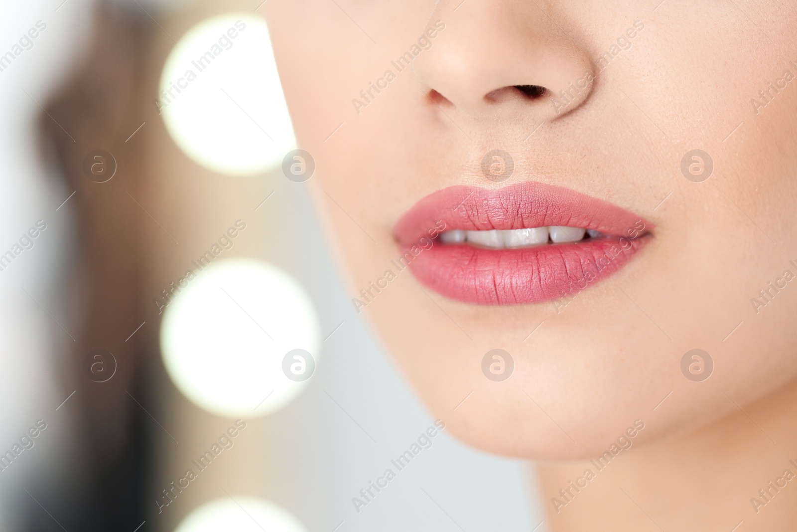 Photo of Young woman wearing beautiful lipstick on blurred background, closeup. Space for text