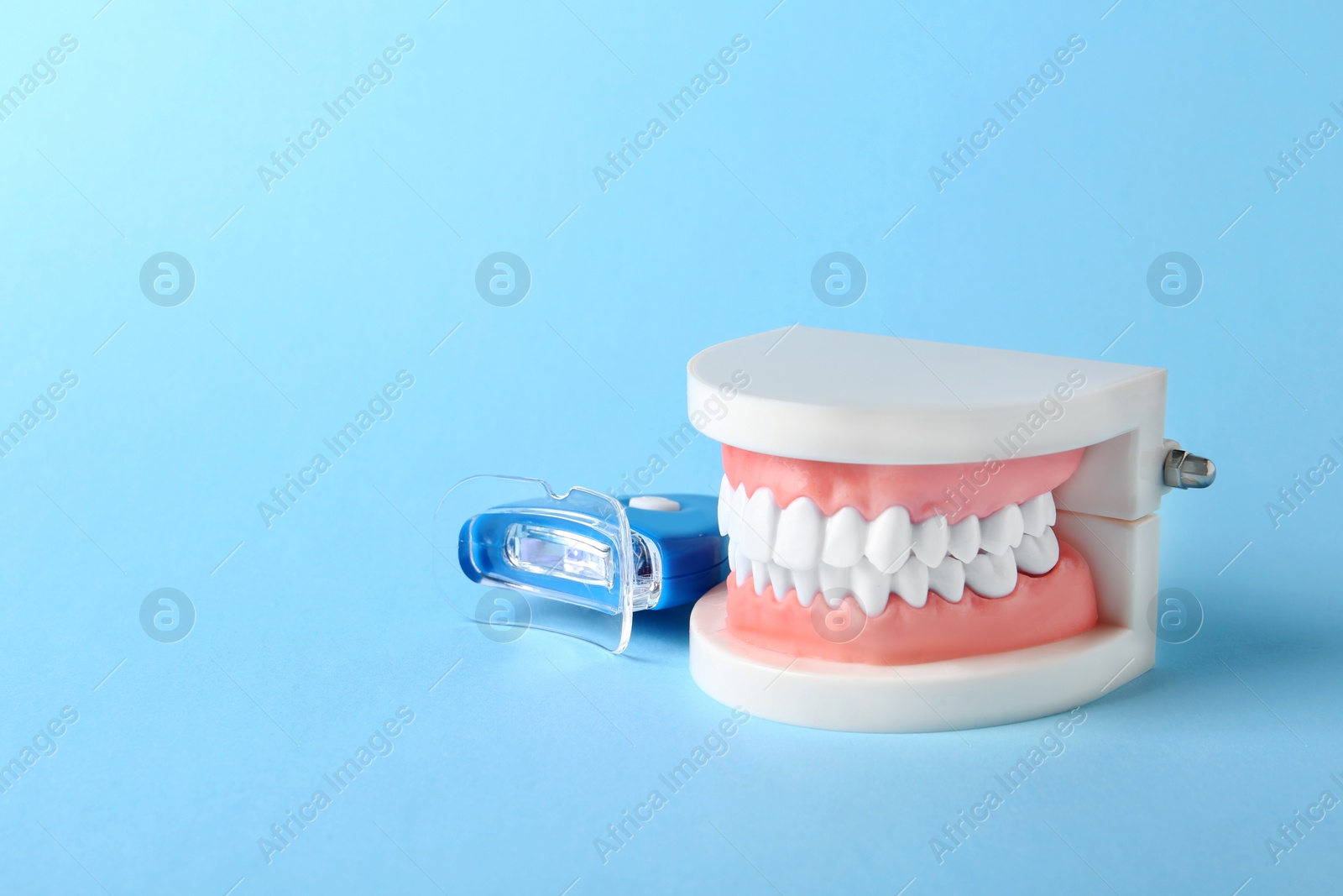 Photo of Educational model of oral cavity with teeth and whitening device on color background. Space for text