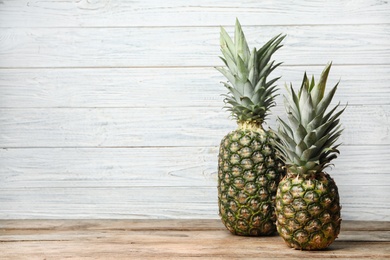 Photo of Fresh delicious pineapples on table against wooden background, space for text