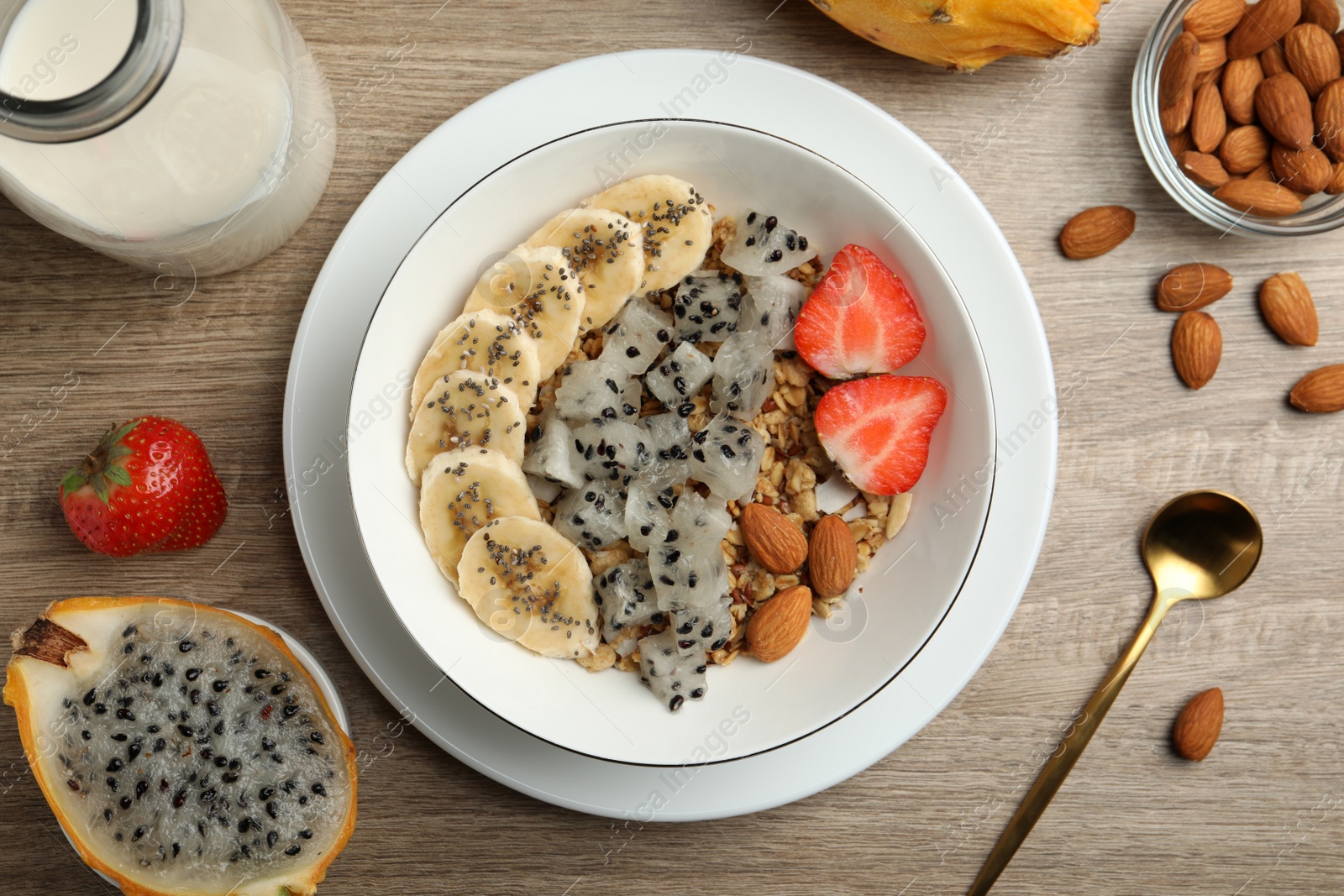 Photo of Bowl of granola with pitahaya, banana, almond and strawberry on wooden table, flat lay