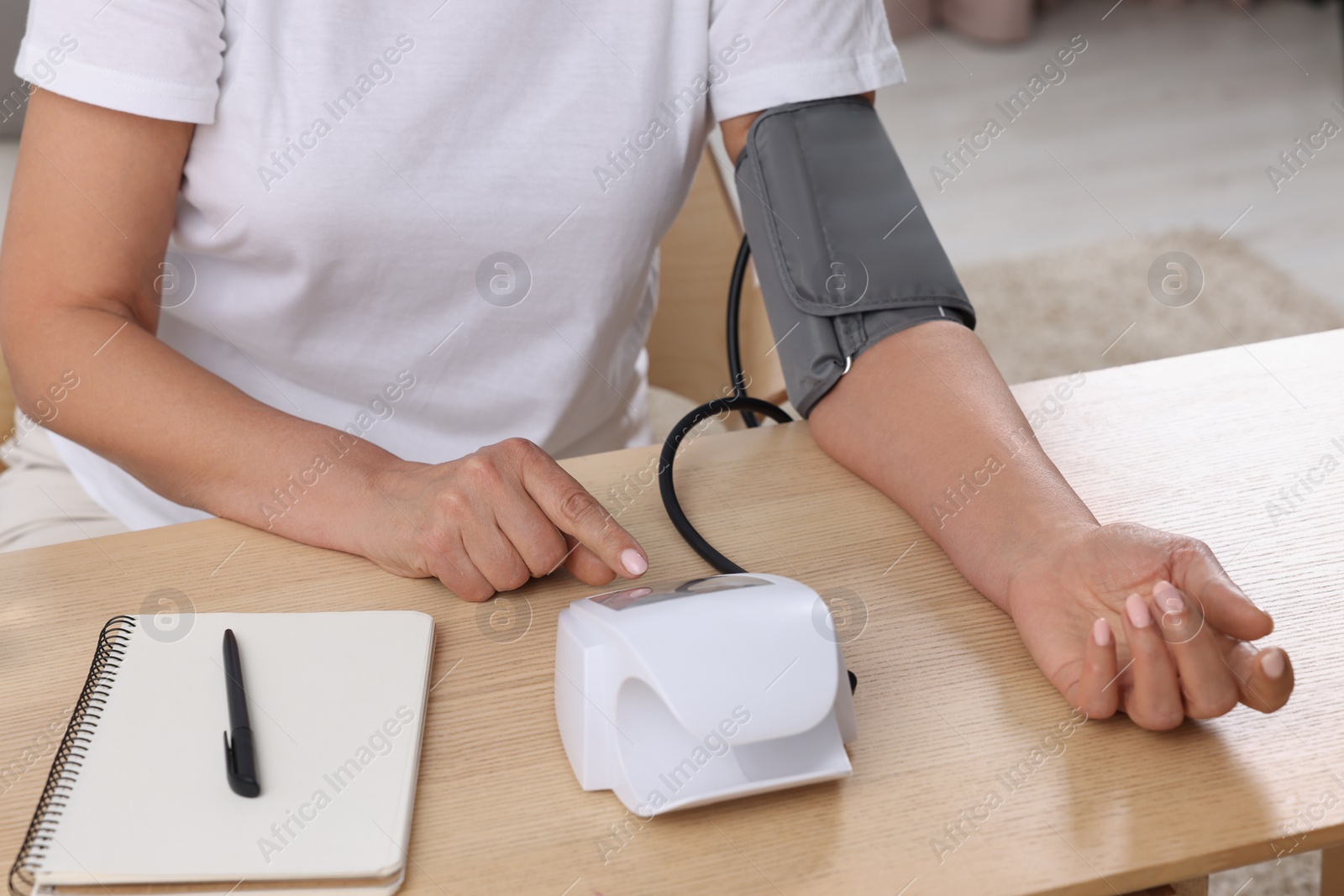 Photo of Woman measuring blood pressure at wooden table indoors, closeup