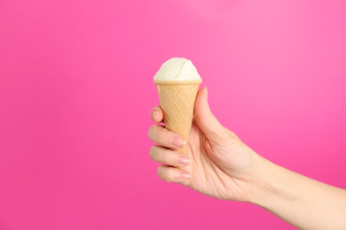 Photo of Woman holding waffle cone with tasty vanilla ice cream on color background