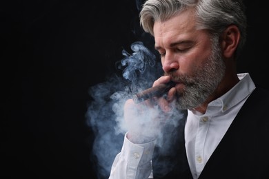 Photo of Bearded man smoking cigar against black background. Space for text