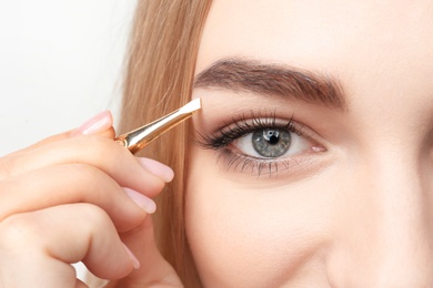 Photo of Young woman plucking eyebrow with tweezers, closeup