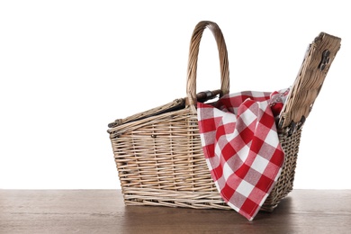 Wicker picnic basket and checkered blanket on wooden table against white background