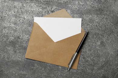 Photo of Envelope with blank paper card and pen on grey table, top view