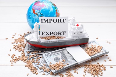 Photo of Card with words Import and Export near globe, wheat grains, money and toy cargo vessel on white wooden table