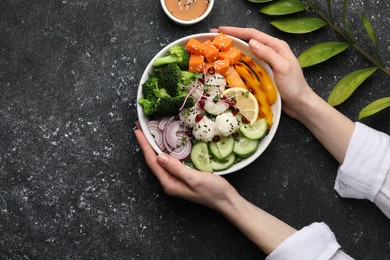 Woman holding bowl with many different vegetables and rice at grey textured table, top view and space for text. Vegan diet