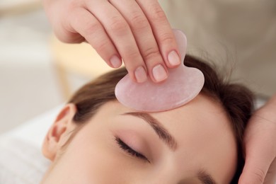 Young woman receiving facial massage with gua sha tool in beauty salon, closeup