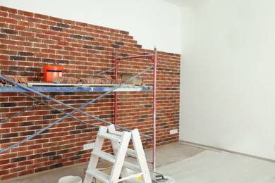 Photo of Scaffolding near wall with decorative bricks and tile leveling system in room