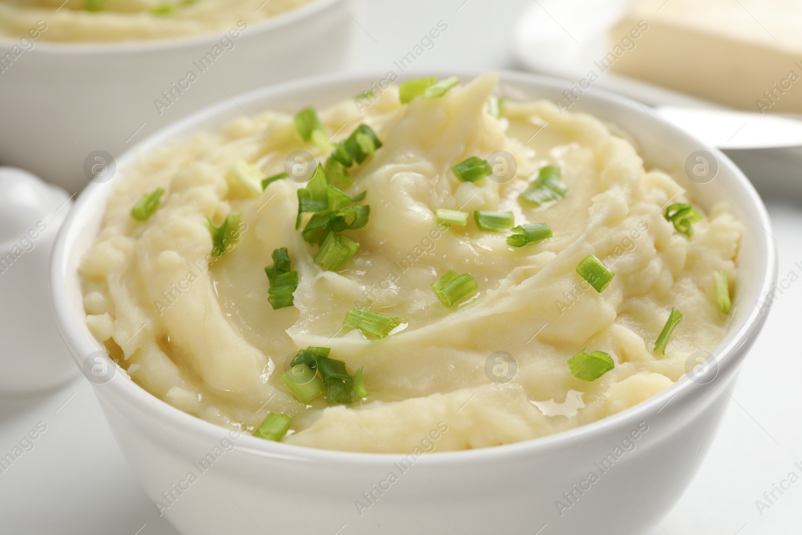 Photo of Bowl of delicious mashed potato with green onion on white table, closeup