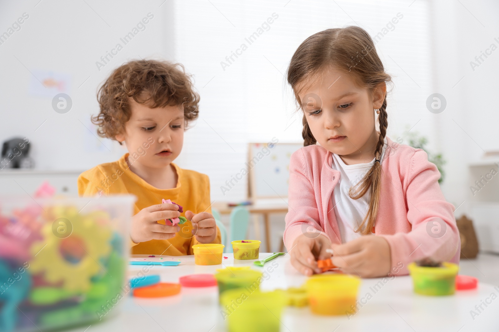 Photo of Cute little children modeling from plasticine at white table in kindergarten