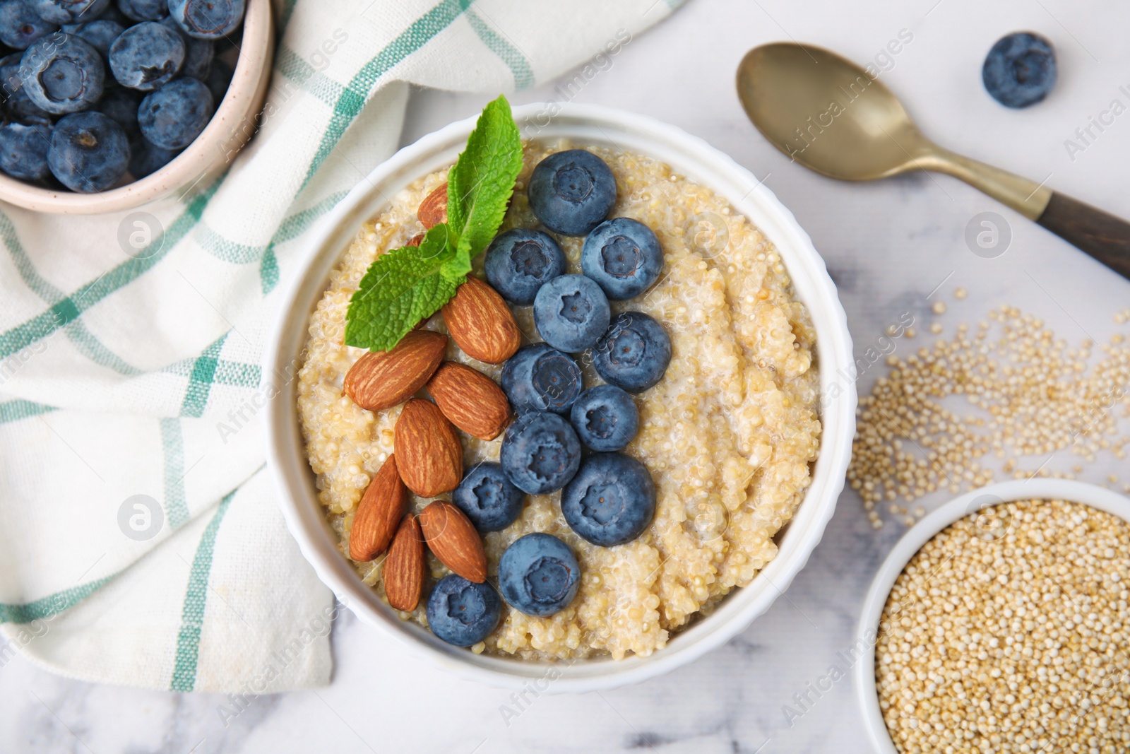 Photo of Bowl of delicious cooked quinoa with almonds and blueberries on white marble table, flat lay